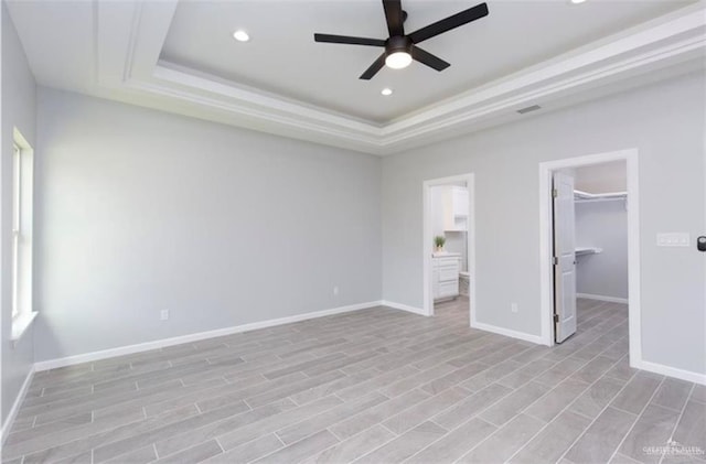 unfurnished bedroom with recessed lighting, baseboards, a spacious closet, and a raised ceiling