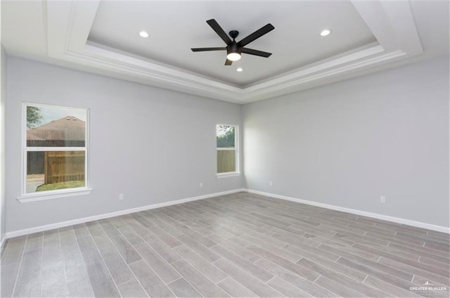 unfurnished room with baseboards, ceiling fan, a tray ceiling, and light wood finished floors