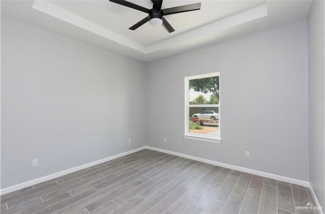 unfurnished room featuring baseboards, a ceiling fan, a raised ceiling, and wood finished floors