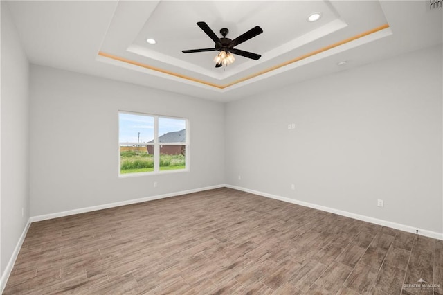 empty room featuring wood-type flooring, a raised ceiling, and ceiling fan