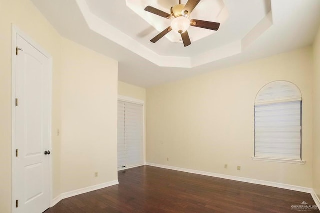 spare room featuring dark hardwood / wood-style flooring, ceiling fan, and a raised ceiling