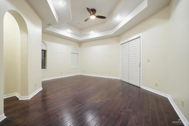 spare room with dark hardwood / wood-style floors, a raised ceiling, and ceiling fan