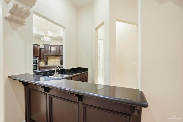 kitchen with a raised ceiling, sink, kitchen peninsula, double oven, and dark brown cabinetry