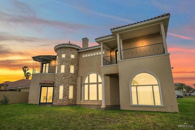 back house at dusk with a balcony and a lawn