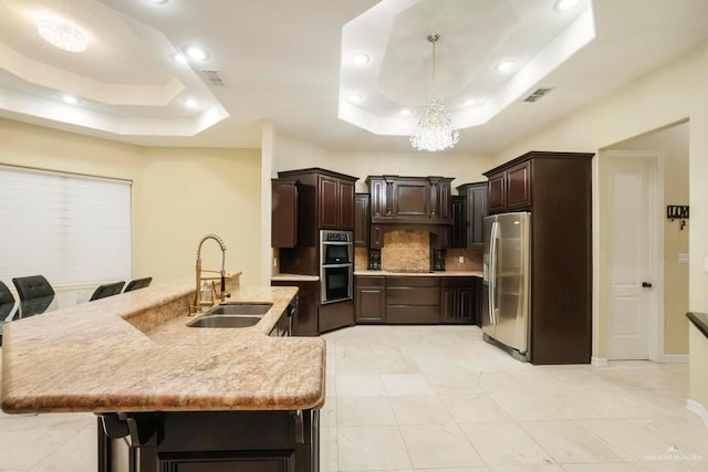 kitchen featuring sink, hanging light fixtures, a tray ceiling, a breakfast bar, and appliances with stainless steel finishes