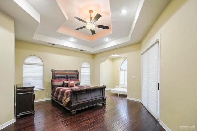 bedroom featuring dark hardwood / wood-style flooring, a tray ceiling, and ceiling fan