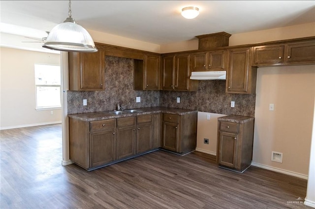 kitchen with a sink, dark wood-style flooring, decorative backsplash, and under cabinet range hood