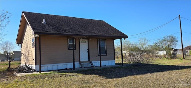 view of front of house with entry steps, roof with shingles, fence, and a front yard