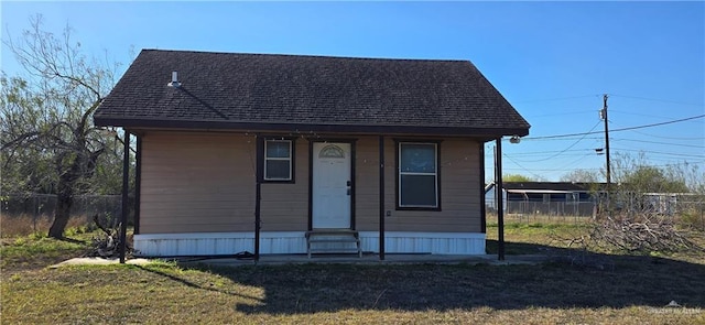 view of front of home with entry steps, roof with shingles, fence, and a front yard