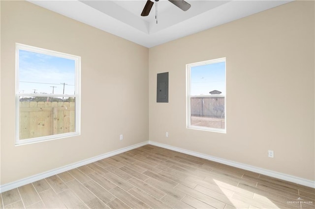 spare room featuring light wood-type flooring, electric panel, ceiling fan, and a tray ceiling