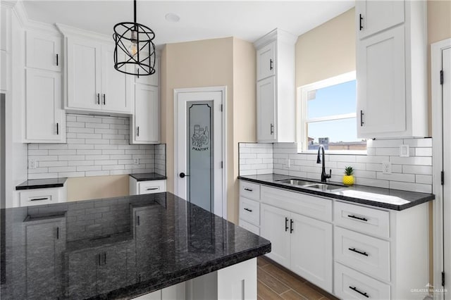 kitchen with pendant lighting, white cabinetry, dark stone counters, and sink