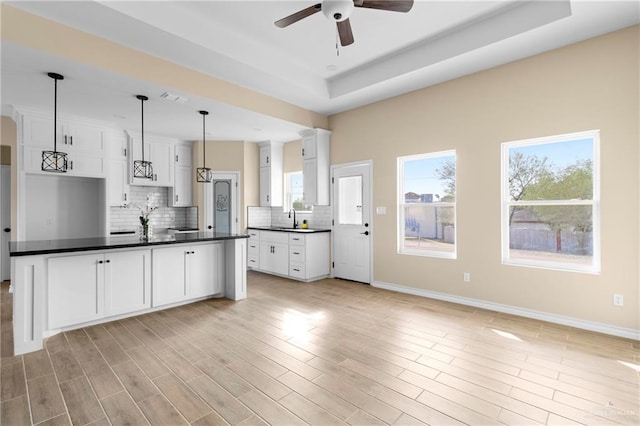 kitchen with white cabinetry, sink, ceiling fan, pendant lighting, and a tray ceiling