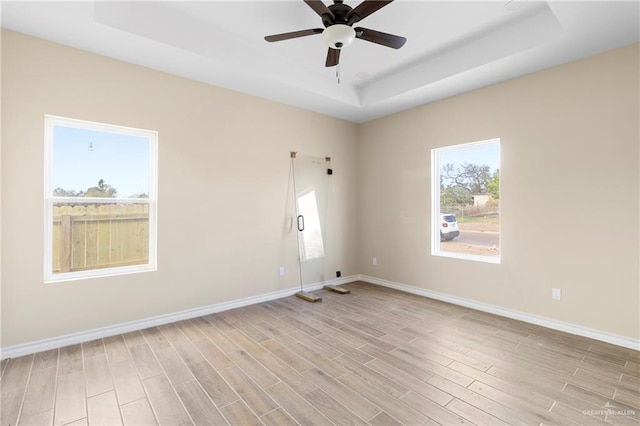 spare room with ceiling fan, a raised ceiling, and light hardwood / wood-style flooring