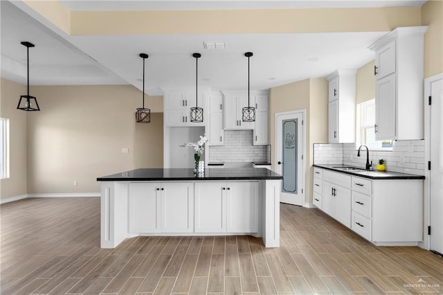 kitchen with white cabinetry, sink, a kitchen island, and pendant lighting