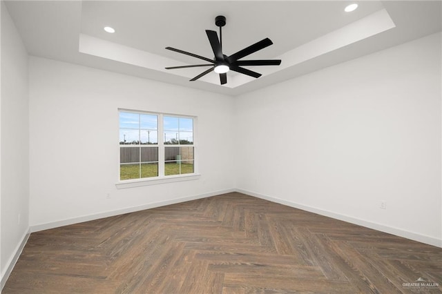 spare room featuring ceiling fan, a raised ceiling, and dark parquet floors