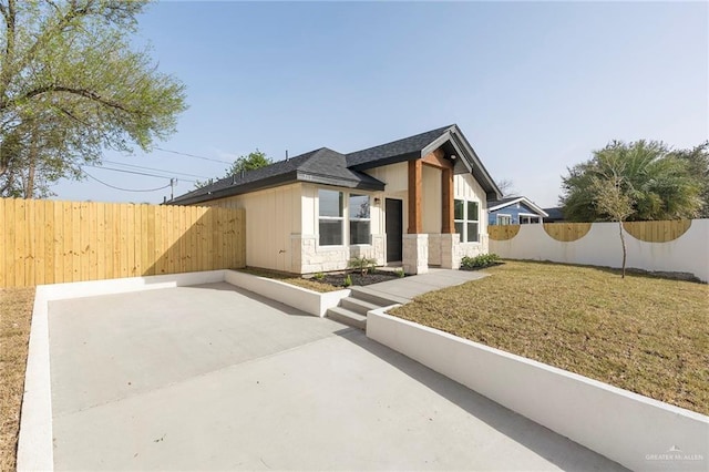 view of front of home featuring stone siding, fence, a front lawn, and a patio