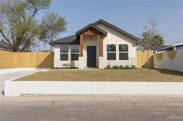 view of front of house featuring stone siding, fence, a front lawn, and board and batten siding