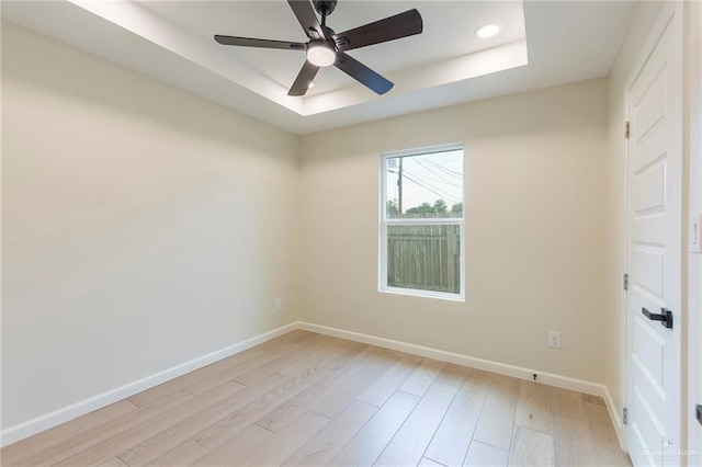 empty room featuring a tray ceiling, baseboards, ceiling fan, and light wood finished floors