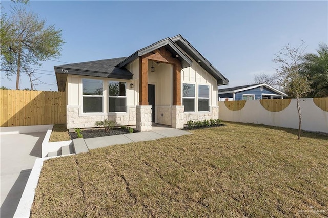 view of front of house with stone siding, board and batten siding, a front yard, and fence