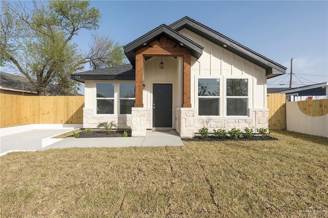 view of front facade with stone siding, fence, board and batten siding, and a front yard