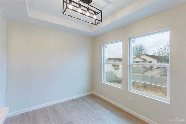 spare room with an inviting chandelier, a raised ceiling, baseboards, and wood finished floors