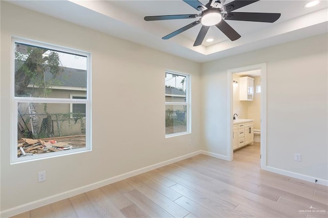 empty room featuring a wealth of natural light, recessed lighting, a raised ceiling, light wood-style flooring, and baseboards