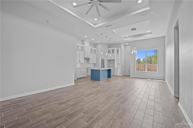 unfurnished living room with hardwood / wood-style floors, ceiling fan with notable chandelier, a raised ceiling, and sink