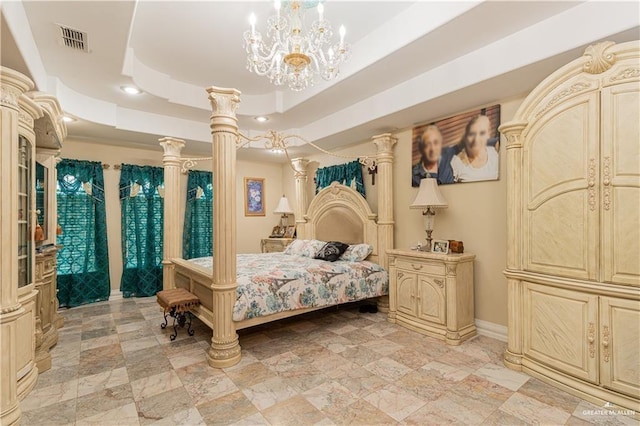 bedroom featuring a tray ceiling, ornate columns, and a chandelier