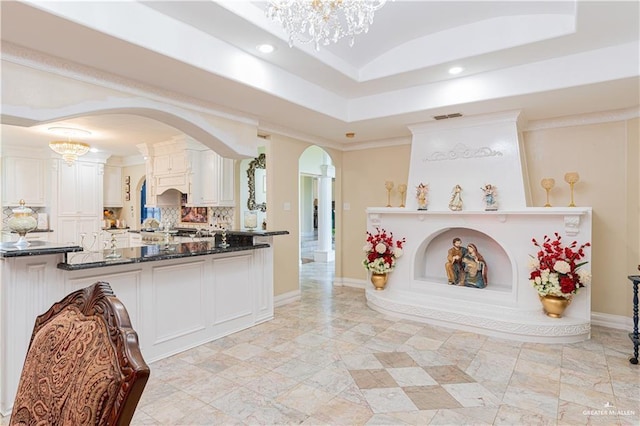 interior space with white cabinetry, backsplash, a chandelier, and dark stone counters