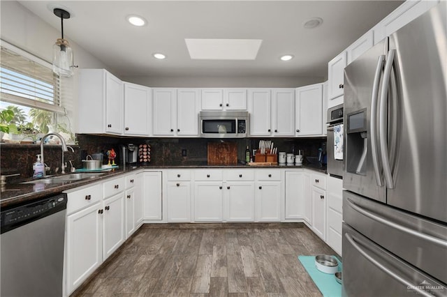 kitchen with sink, a skylight, appliances with stainless steel finishes, decorative light fixtures, and light hardwood / wood-style floors