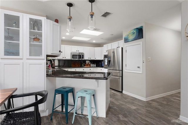 kitchen featuring white cabinetry, stainless steel appliances, a kitchen breakfast bar, dark hardwood / wood-style floors, and kitchen peninsula