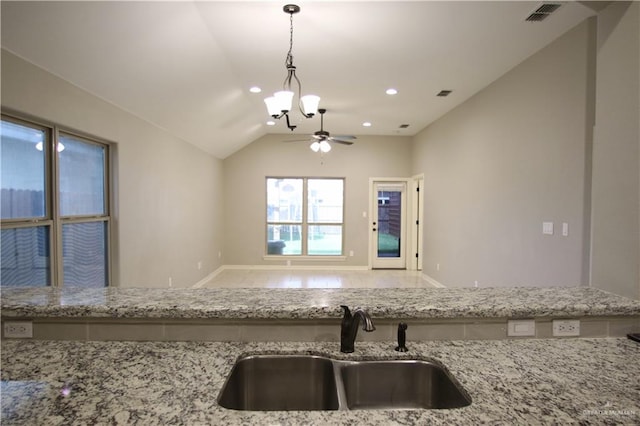 kitchen with lofted ceiling, ceiling fan with notable chandelier, sink, hanging light fixtures, and light stone countertops