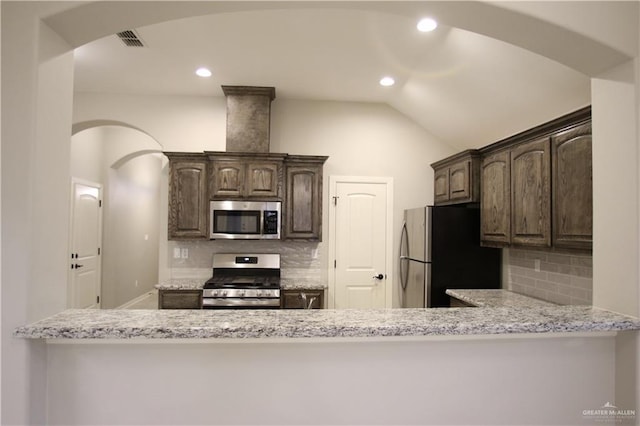 kitchen featuring light stone countertops, backsplash, stainless steel appliances, and lofted ceiling