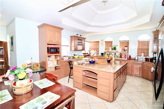 kitchen with light brown cabinetry, a raised ceiling, a kitchen island, and light tile patterned floors