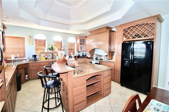 kitchen with a kitchen breakfast bar, kitchen peninsula, light tile patterned flooring, black fridge with ice dispenser, and a raised ceiling