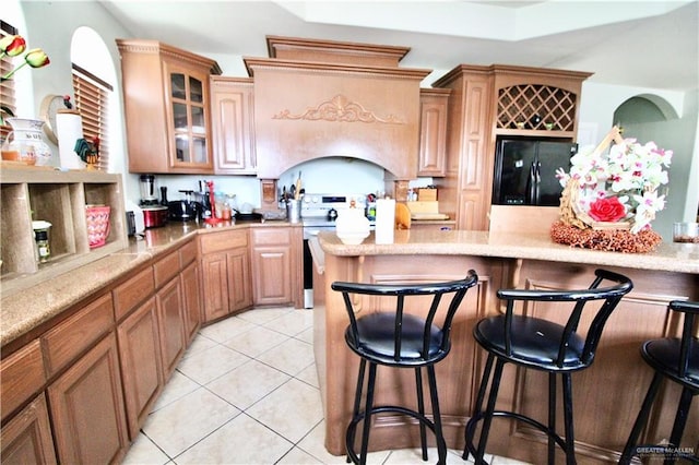 kitchen featuring electric stove, a breakfast bar, light stone countertops, light tile patterned flooring, and black fridge