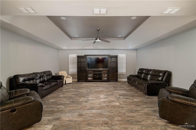 living room with ceiling fan, a raised ceiling, and wood-type flooring