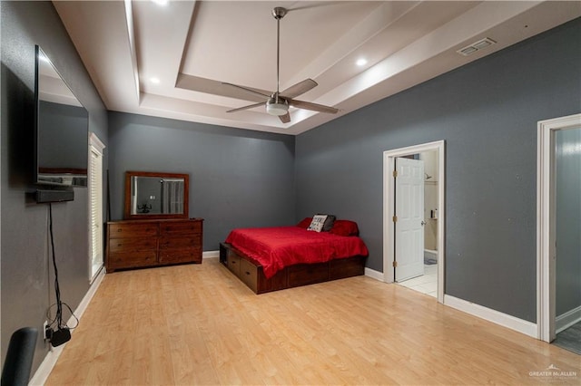 bedroom featuring a tray ceiling, ceiling fan, light hardwood / wood-style floors, and ensuite bathroom