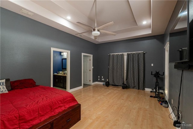 bedroom with connected bathroom, a tray ceiling, ceiling fan, and light hardwood / wood-style floors