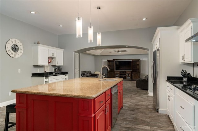 kitchen with ceiling fan, sink, dark stone countertops, white cabinetry, and an island with sink