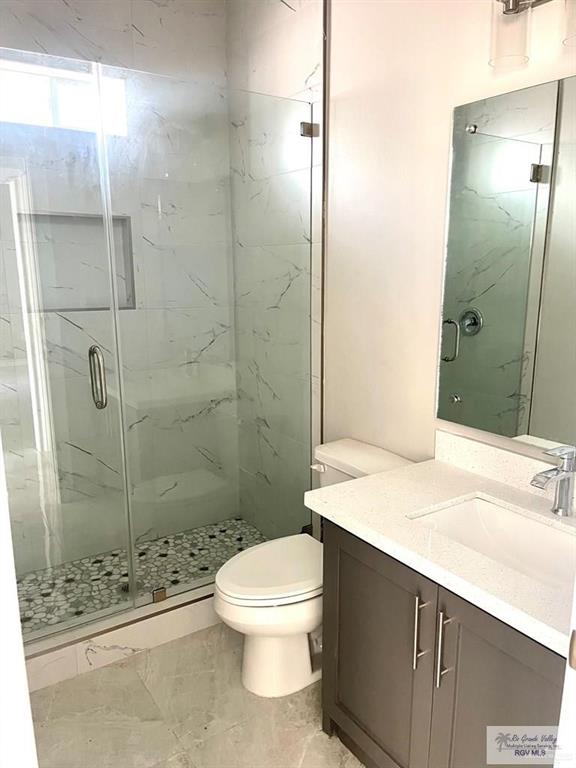 full bath with toilet, a marble finish shower, and vanity