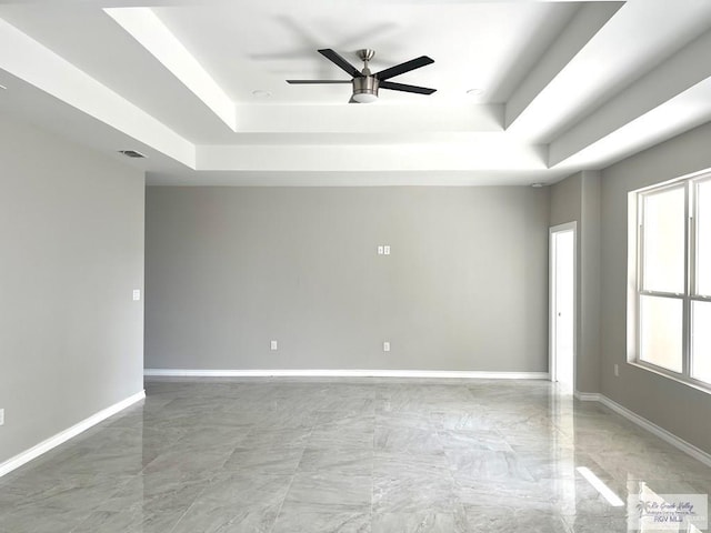 unfurnished room featuring ceiling fan, a tray ceiling, and baseboards