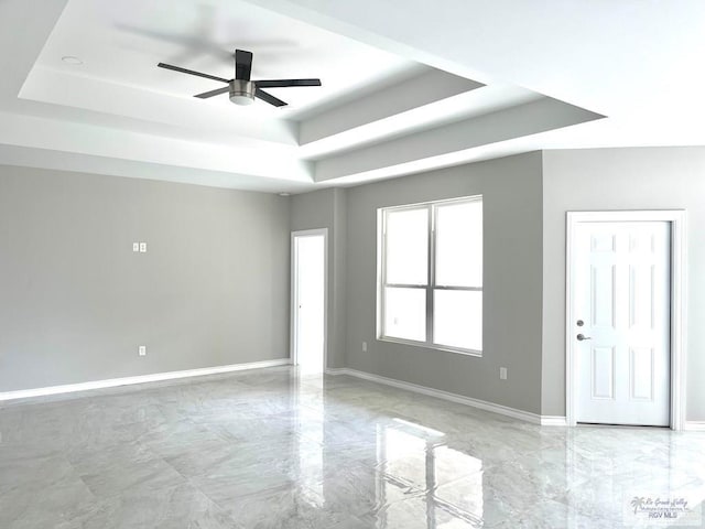 spare room featuring marble finish floor, baseboards, a tray ceiling, and ceiling fan