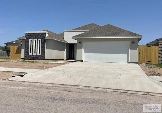 view of front of home featuring a garage, driveway, roof with shingles, fence, and stucco siding