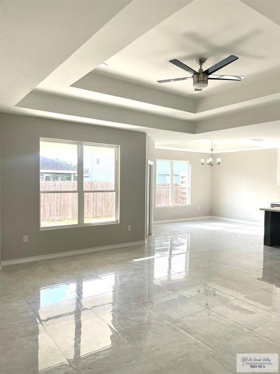 spare room with ceiling fan with notable chandelier, a raised ceiling, and baseboards