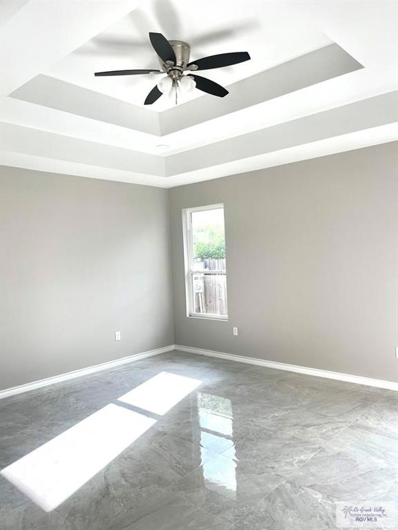 spare room with a raised ceiling, ceiling fan, marble finish floor, and baseboards