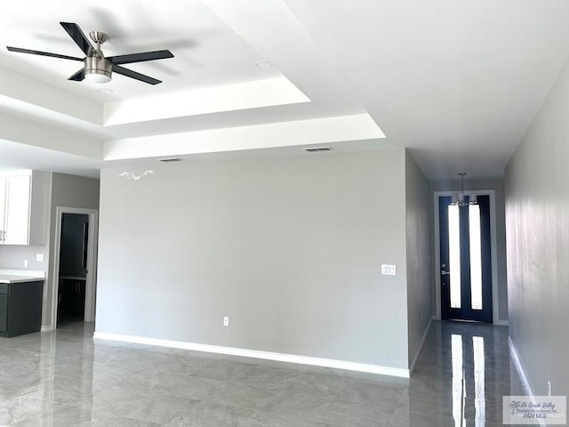 spare room featuring visible vents, a tray ceiling, baseboards, and ceiling fan with notable chandelier