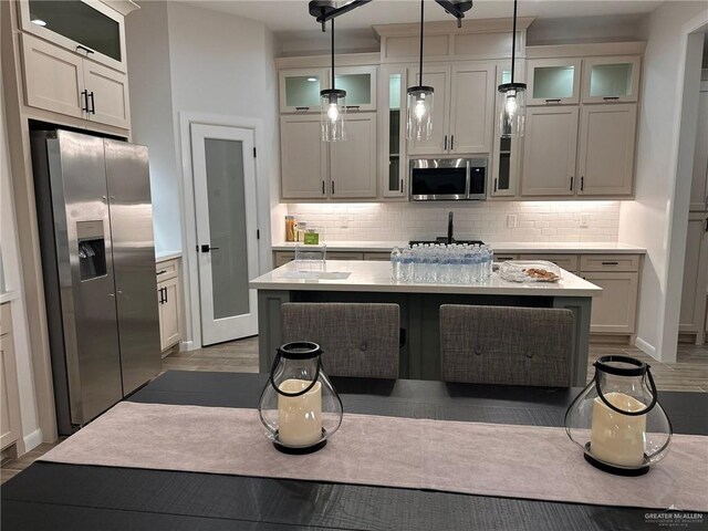 kitchen featuring decorative backsplash, appliances with stainless steel finishes, a kitchen island with sink, and pendant lighting