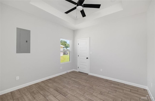 empty room featuring ceiling fan, light hardwood / wood-style floors, electric panel, and a tray ceiling