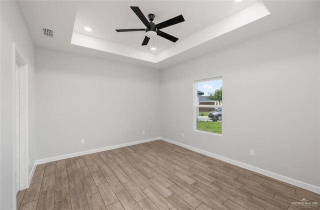 empty room featuring a tray ceiling, ceiling fan, and light hardwood / wood-style floors